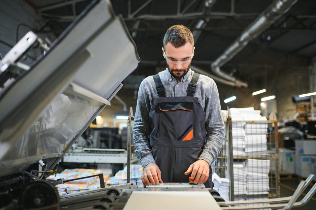 Printing house interior with modern offset print machine and operator in working uniform